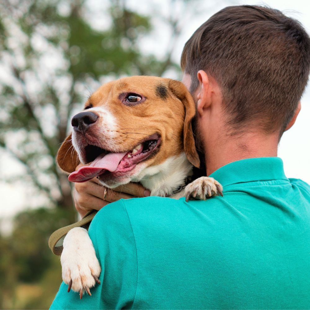 A man stands outdoors, gently holding a dog in his arms